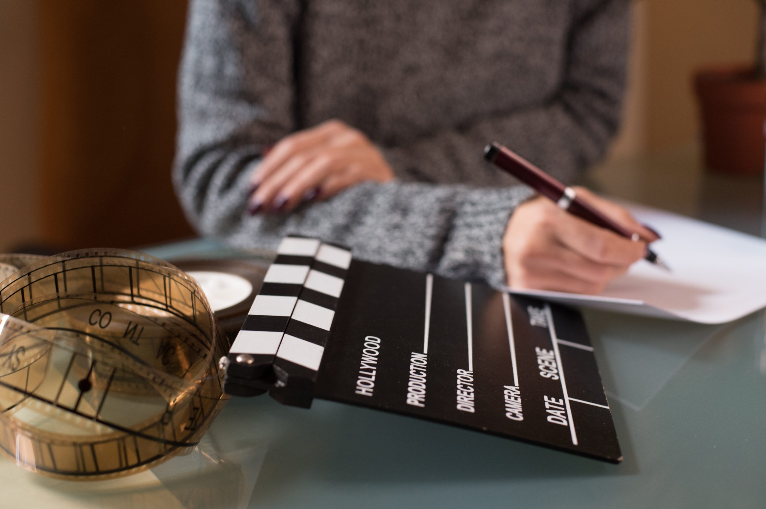Artist Screenwriter Desktop Detail With Movie Clapper Board And Filmstrip With Woman's Hand Working In Background